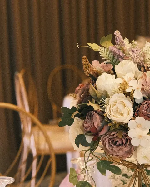 A bouquet of ivory and dusty-rose flowers on a gold stand above a table with blush napkins