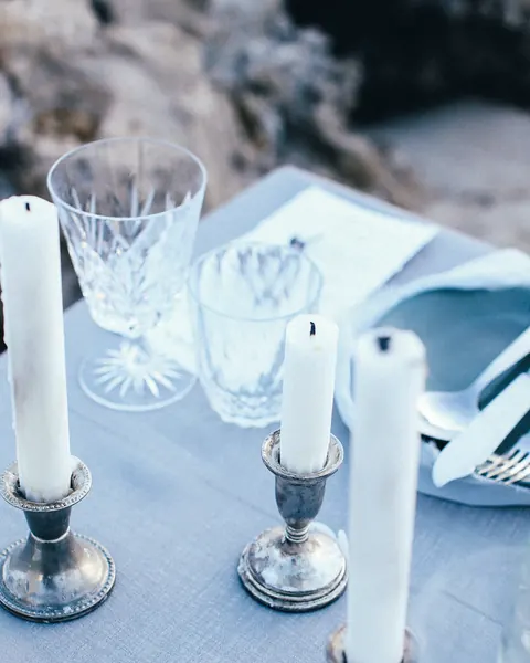Tall white candles in silver holders and crystal glasses on a blue linen