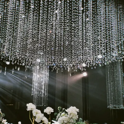 Strands of crystal falling from the ceiling, catching beams of light above white flowers
