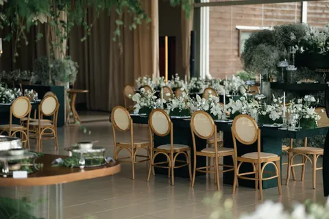 Long emerald tables with white flowers and candles, and wooden cane-back chairs