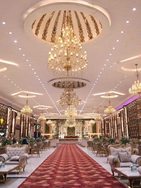 A wedding hall with a row of gold crystal chandeliers, a long aisle and sofa seating on both sides