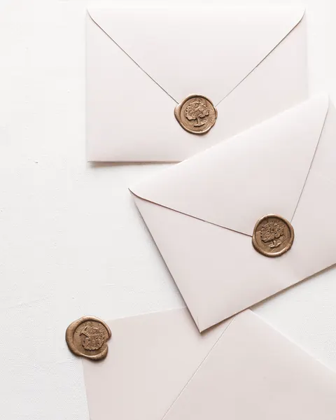 Pale blush invitation envelopes closed with gold wax seals