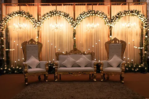 A kosha of four white-flower arches before lit drapes, with a gilded sofa and two chairs
