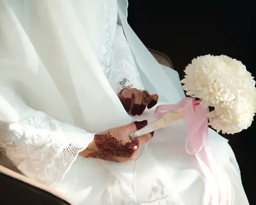 A bride’s henna-painted hands holding a white bouquet tied with a blush ribbon
