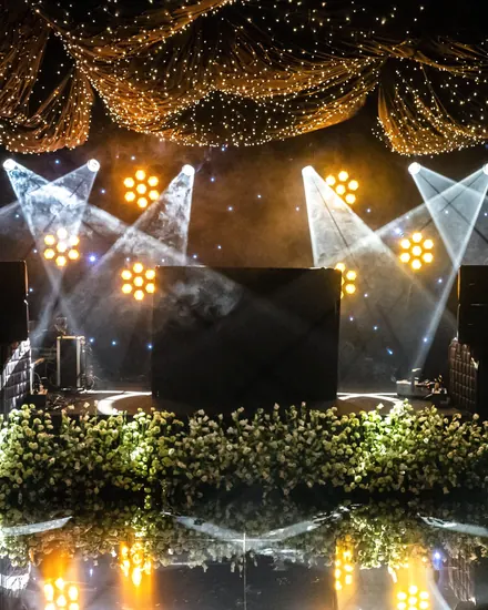 An event stage with moving lights, a starlit fabric ceiling and a bank of white flowers